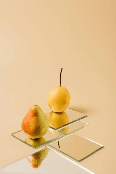 Две желтые груши отражаются в зеркалах на бежевом столе — стоковое фото