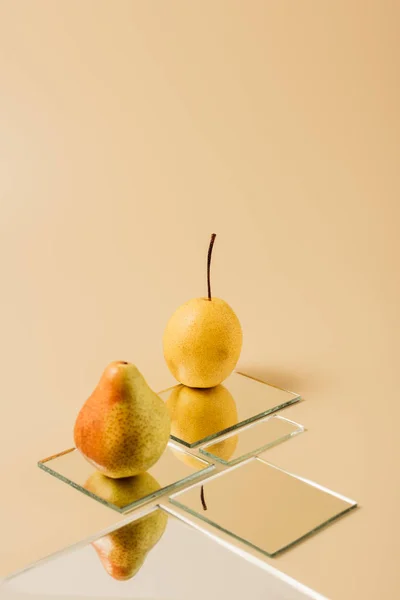 Two yellow pears reflecting in mirrors on beige table — Stock Photo
