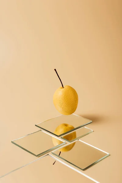 Una pera amarilla reflejándose en espejos sobre una mesa beige - foto de stock