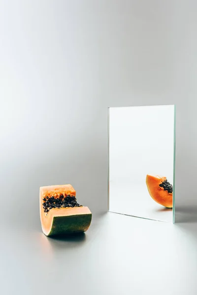 Una pieza de papaya reflejándose en el espejo sobre la mesa blanca - foto de stock