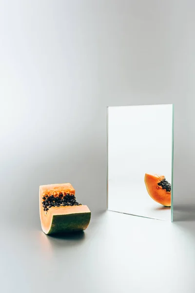 One piece of papaya reflecting in mirror on white table — Stock Photo