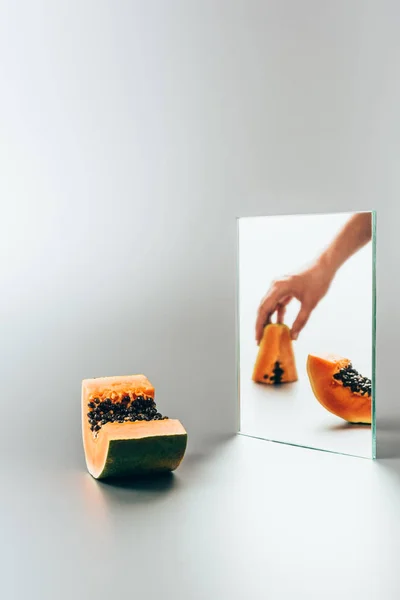 Abgeschnittenes Bild einer Frau mit gelber Papaya, die im Spiegel auf weißem Tisch reflektiert — Stockfoto