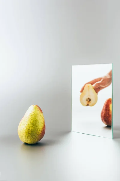 Cropped image of woman holding yellow pear reflecting in mirror on white surface — Stock Photo