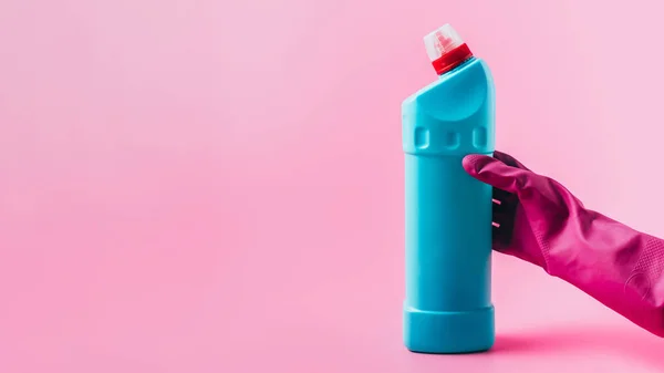 Imagen recortada de limpiador femenino en guante de goma que sostiene el fluido de limpieza, fondo rosa - foto de stock