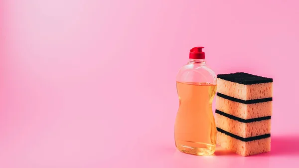 Close up view of dishwashing liquid and stack of washing sponges, pink background — Stock Photo