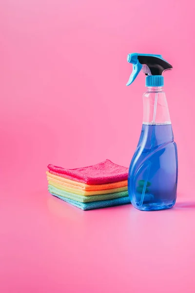 Vista de perto do fluido de limpeza e pilha de trapos coloridos, fundo rosa — Fotografia de Stock