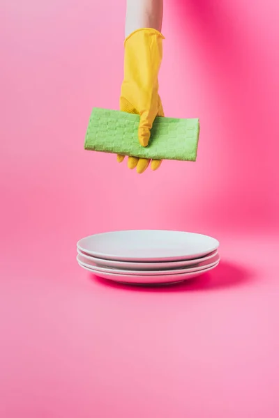 Cropped image of woman holding cleaning napkin over stack of clean white plates, pink background — Stock Photo