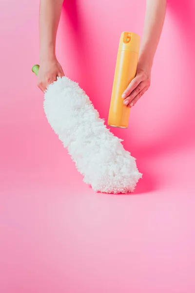 Imagem cortada de limpador feminino segurando lata de pulverização e espanador branco, fundo rosa — Fotografia de Stock