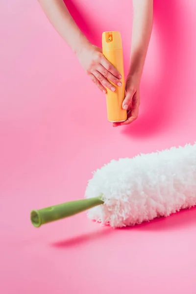 Vista parcial del limpiador femenino que sostiene el aerosol puede cerca del plumero blanco, fondo rosa - foto de stock