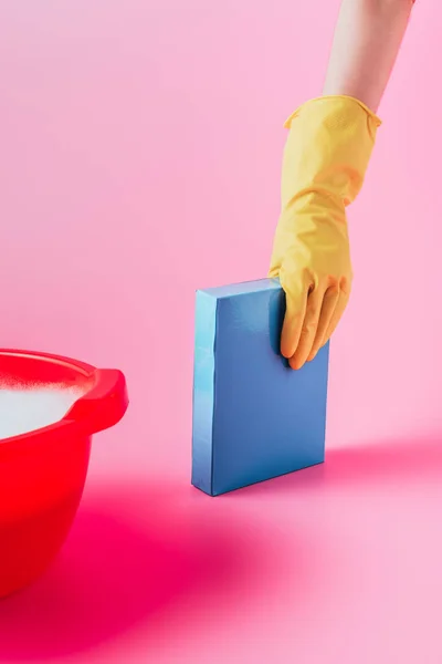 Immagine ritagliata della donna in guanto di gomma che prende polvere di lavaggio vicino al bacino di plastica con schiuma, sfondo rosa — Foto stock