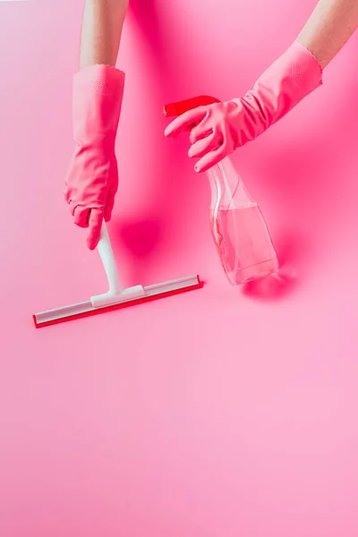 Cropped image of female cleaner in rubber gloves cleaning floor by squeegee with cleaning fluid, pink background — Stock Photo