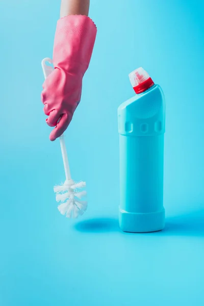 Image recadrée du nettoyant féminin tenant la brosse de toilette près du liquide de nettoyage, fond bleu — Photo de stock