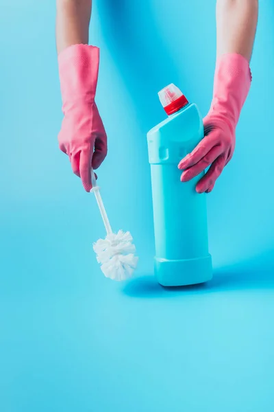 Partial view of female cleaner holding cleaning fluid and toilet brush, blue background — Stock Photo