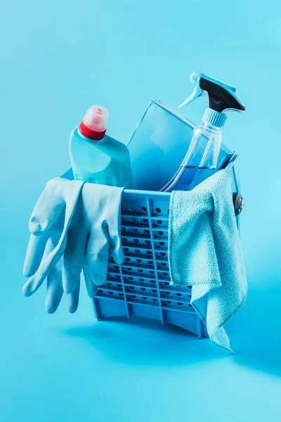 Vista de cerca del cubo con polvo de lavado, líquidos de limpieza, guantes de goma y trapo sobre fondo azul - foto de stock