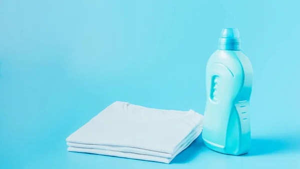 Close up view of laundry liquid and stack of white clean t-shirts, blue background — Stock Photo