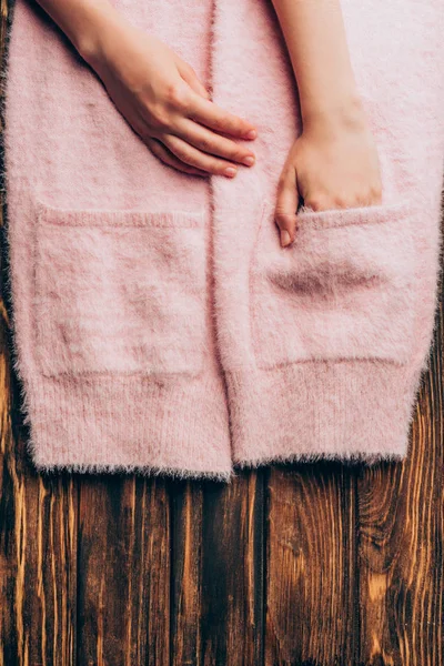 Immagine ritagliata donna mettendo le mani in tasche di maglione rosa su tavolo in legno — Foto stock