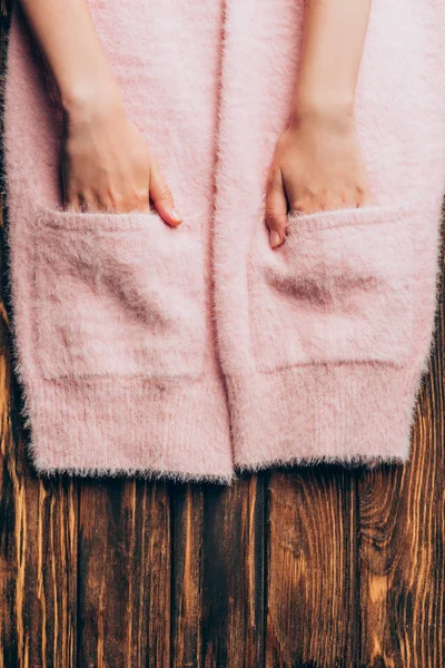 Abgeschnittenes Image-Mädchen legt Hände in Taschen aus rosa Pullover auf Holztisch — Stockfoto