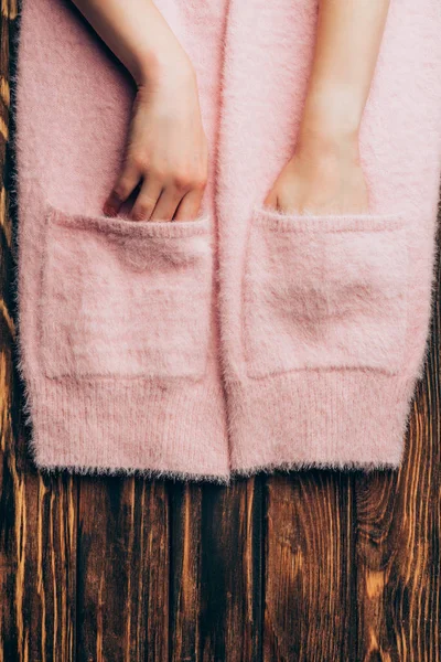 Cropped image woman putting hands in pockets of pink sweater on wooden table — Stock Photo