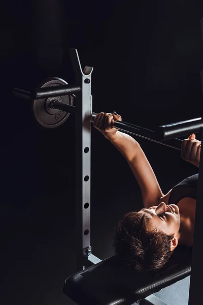 Vista de ángulo alto del culturista femenino haciendo ejercicio con barra de pesas en el gimnasio, fondo negro - foto de stock