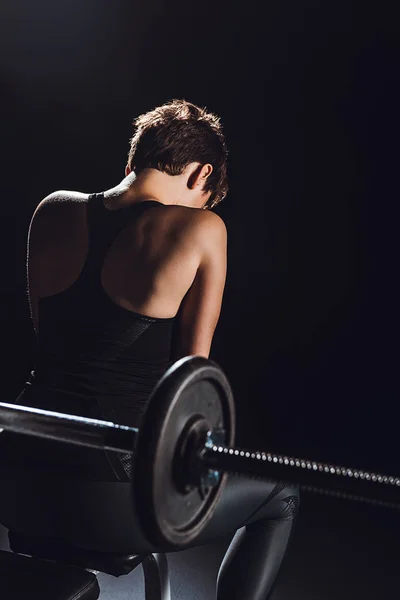 Visão traseira do atleta esportivo feminino descansando perto de barbell, fundo preto — Fotografia de Stock