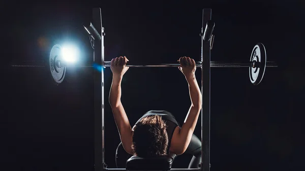 Жінка-бодибилдерша вправа з барбелом в спортзалі, чорний фон — стокове фото