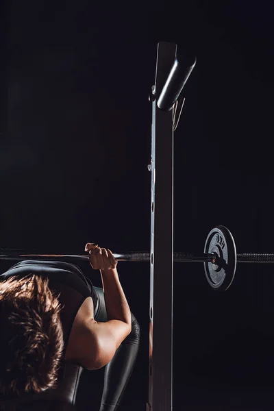 Vista parziale di atleta donna che fa esercizio fisico con bilanciere, sfondo nero — Foto stock