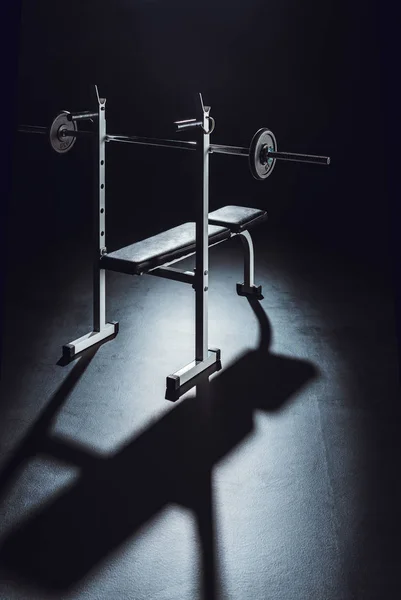 Barbell with shadow on floor at gym, black background — Stock Photo