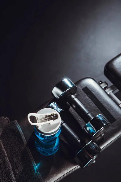 Vue du dessus de la bouteille de sport, serviette, haltères à la salle de gym, fond noir — Photo de stock