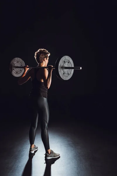 Vista posteriore di giovane atleta donna che si allena con bilanciere, sfondo nero — Foto stock