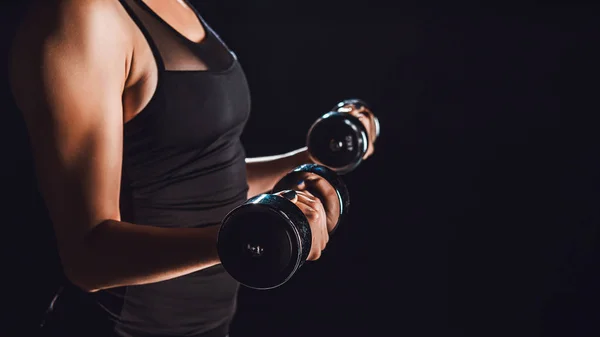 Partial view of female bodybuilder working out with dumbbells, black background — Stock Photo