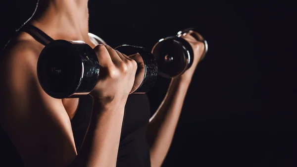 Imagen recortada de la atleta haciendo ejercicio con pesas, fondo negro - foto de stock