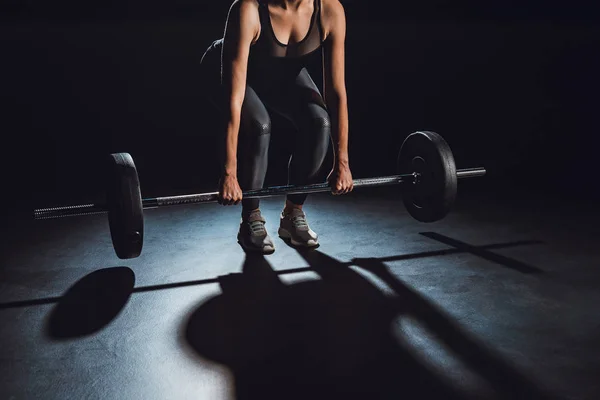 Частичный взгляд спортсменки упражнения с штангой в тренажерном зале, черный фон — стоковое фото