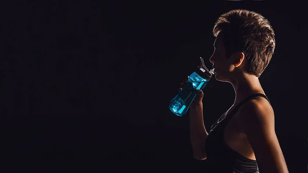 Side view of sportswoman drinking water from bottle, black background — Stock Photo