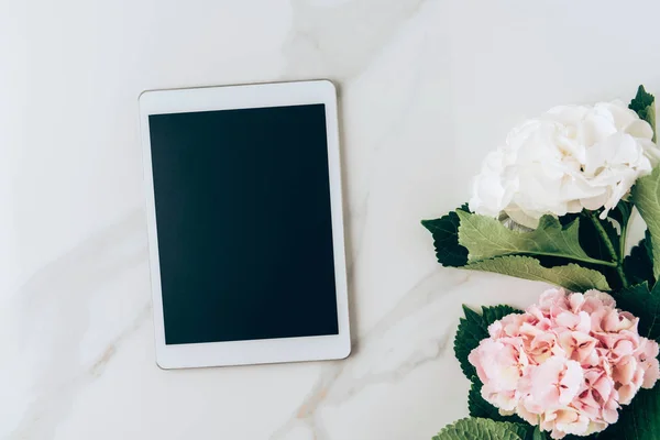 Vista superior de la tableta digital con pantalla en blanco y flores de hortensia sobre fondo de mármol - foto de stock
