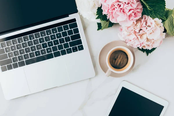 Cama plana con taza de café, portátil, tableta digital y flores de hortensias en la superficie de mármol - foto de stock