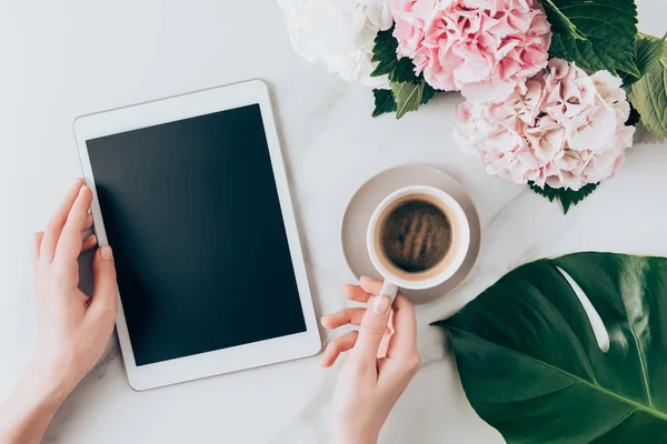 Abgeschnittene Ansicht der Frauenhand mit Kaffeetasse und digitalem Tablet mit leerem Bildschirm auf Tabletop mit Hortensienblüten — Stockfoto