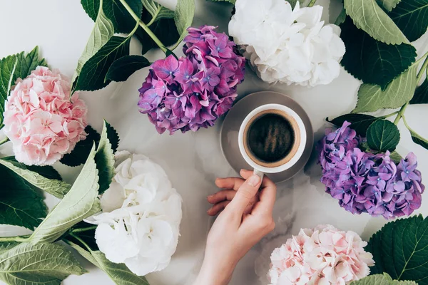 Плоская лежала с цветами гортензии и женской рукой с чашкой кофе эспрессо — стоковое фото