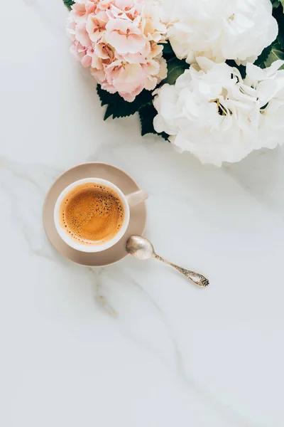 Верхний вид чашки с кофе эспрессо и ложкой на мраморной поверхности с красивыми цветами гортензии — стоковое фото