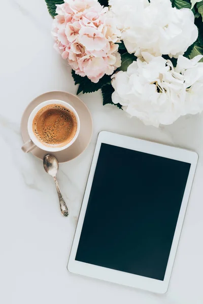 Vue du dessus de la tasse avec café expresso, fleurs d'hortensia et tablette numérique avec écran blanc sur la surface du marbre — Photo de stock