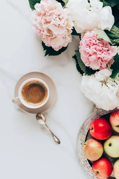 Flat lay with coffee cup, spoon, apples and pink hortensia flowers on marble surface — Stock Photo