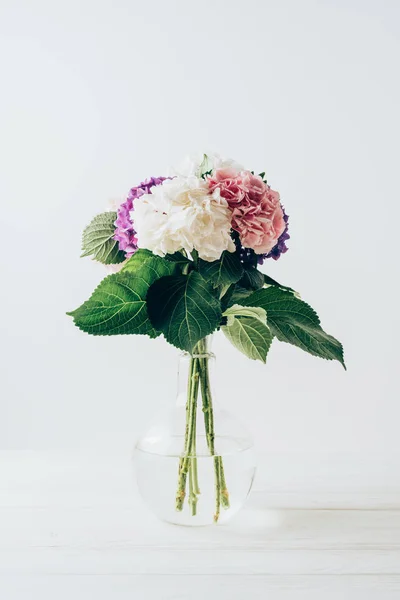 Beautiful colorful hydrangea flowers in glass vase, on white — Stock Photo