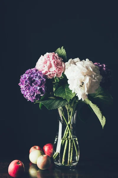 Rosa, flor branca e roxa em vaso de vidro com maçãs, em preto — Fotografia de Stock