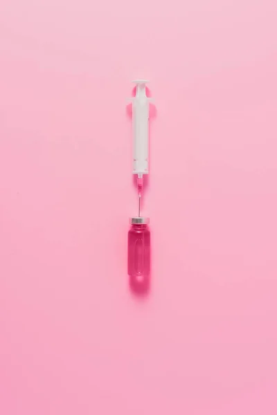 Top view of syringe with ampule of pink liquid on pink surface — Stock Photo