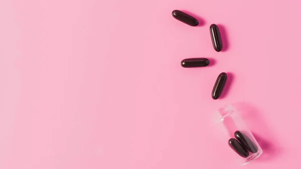 Vista superior de las cápsulas médicas negras derramadas del frasco sobre rosa — Stock Photo