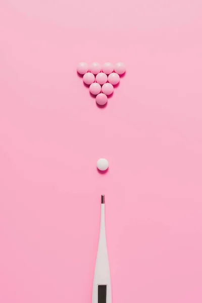 Top view of pills with electric thermometer arranged in billiard composition on pink — Stock Photo