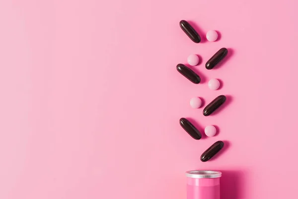 Vista superior de lata con píldoras dispuestas de color rosa y negro en rosa - foto de stock