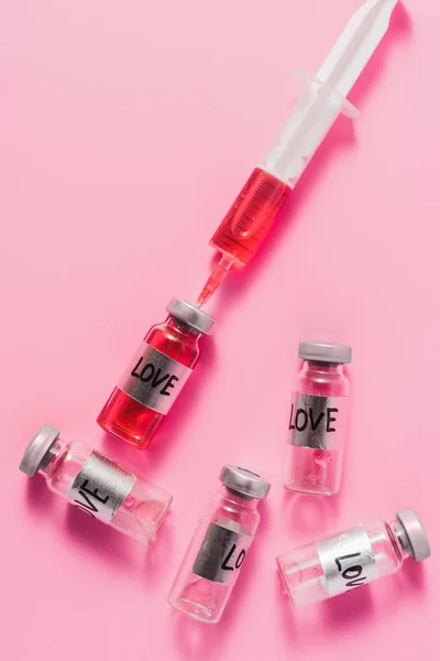 Vista superior da seringa e frascos com sinais de vacina contra o amor no tampo rosa — Fotografia de Stock