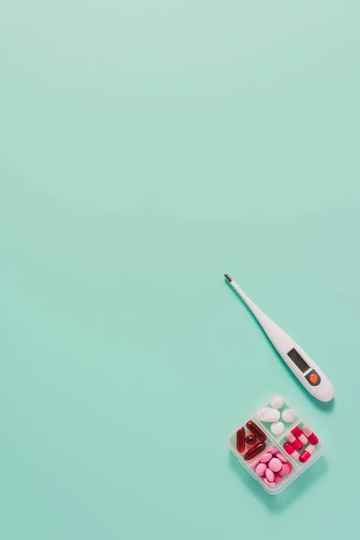 Top view of plastic container with various sorted pills and electric thermometer on blue — Stock Photo