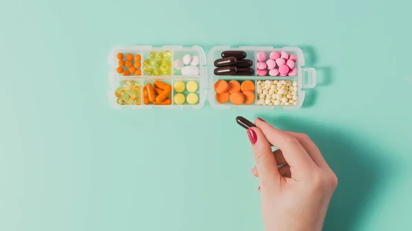 Cropped shot of woman taking capsule from plastic case with various sorted pills on blue — Stock Photo