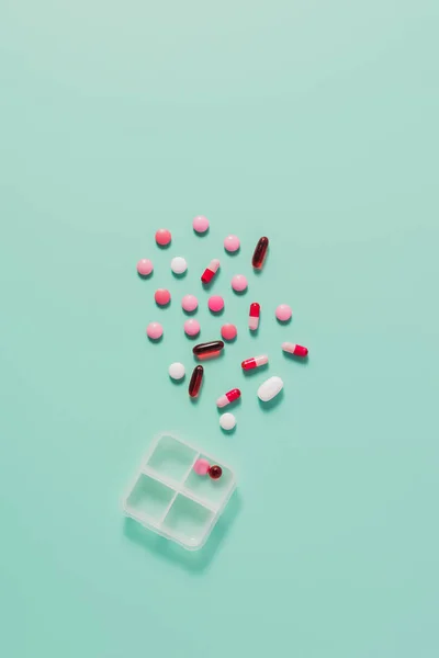 Top view of various pills spilled from plastic case on blue — Stock Photo